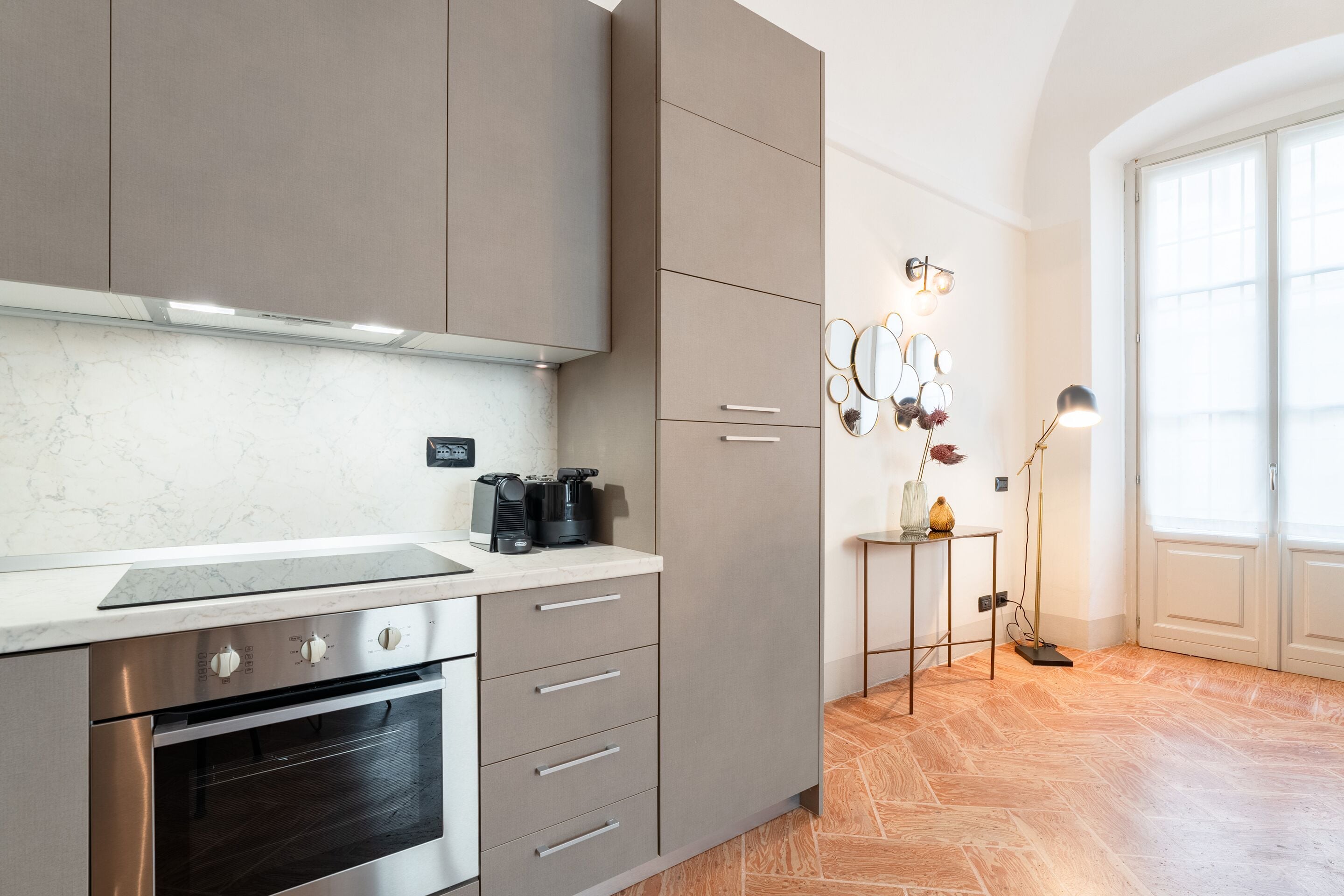 A modern kitchen with stainless steel appliances, a marble countertop, and a herringbone wood floor.