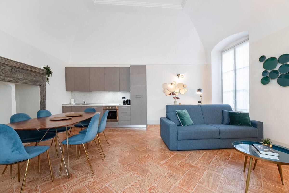 Un salon moderne avec un canapé bleu, une table à manger et des chaises, et une cuisine en arrière-plan.