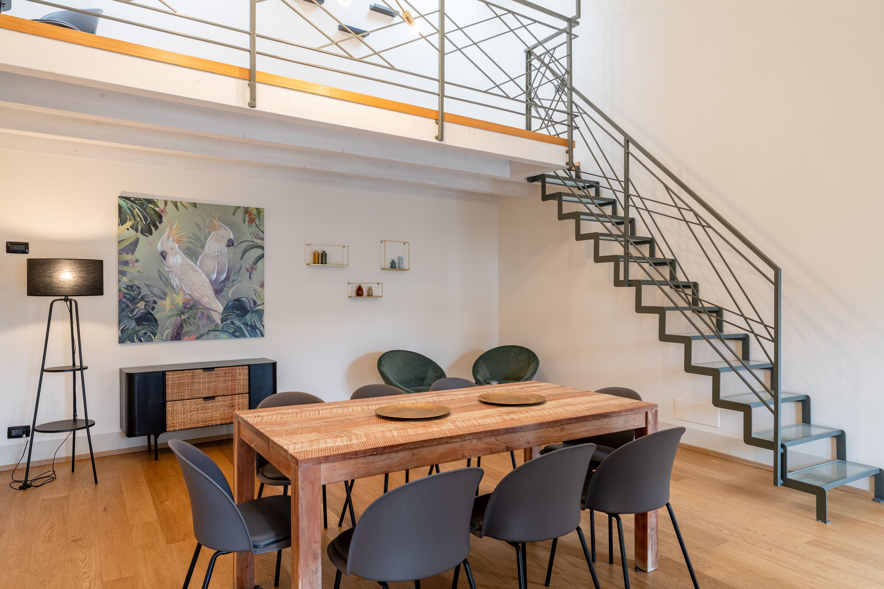 A modern dining area with a wooden table, black chairs, a painting, and a staircase.