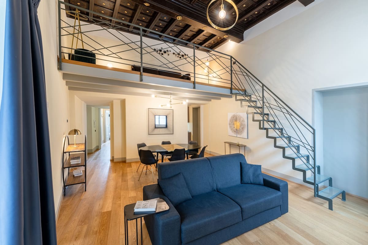 Un vaste espace de vie agrémenté d’un escalier moderne, d’un canapé bleu et d’une table à manger.