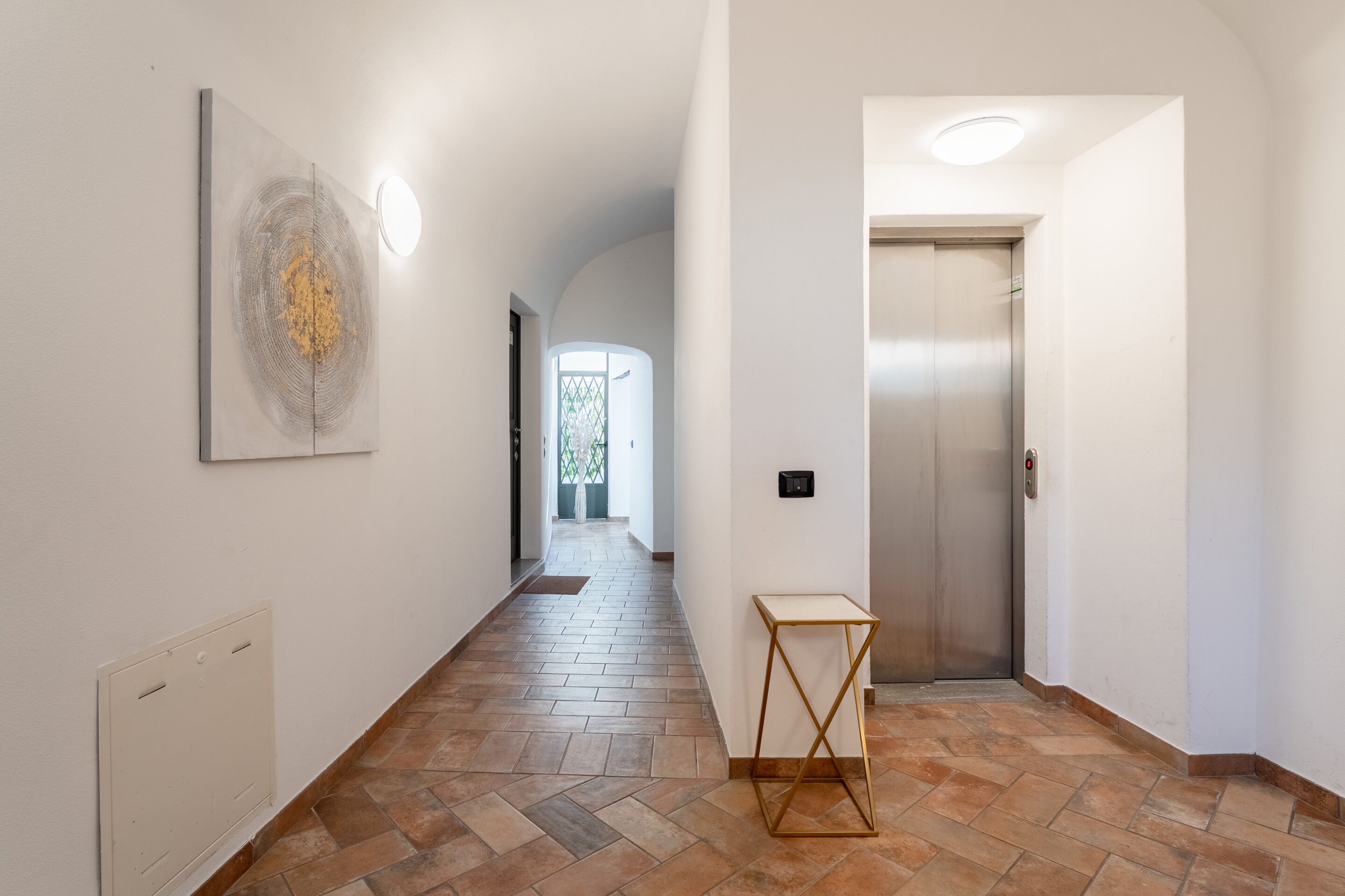 A hallway with a tiled floor, a wall-mounted artwork, a small table, and an elevator.