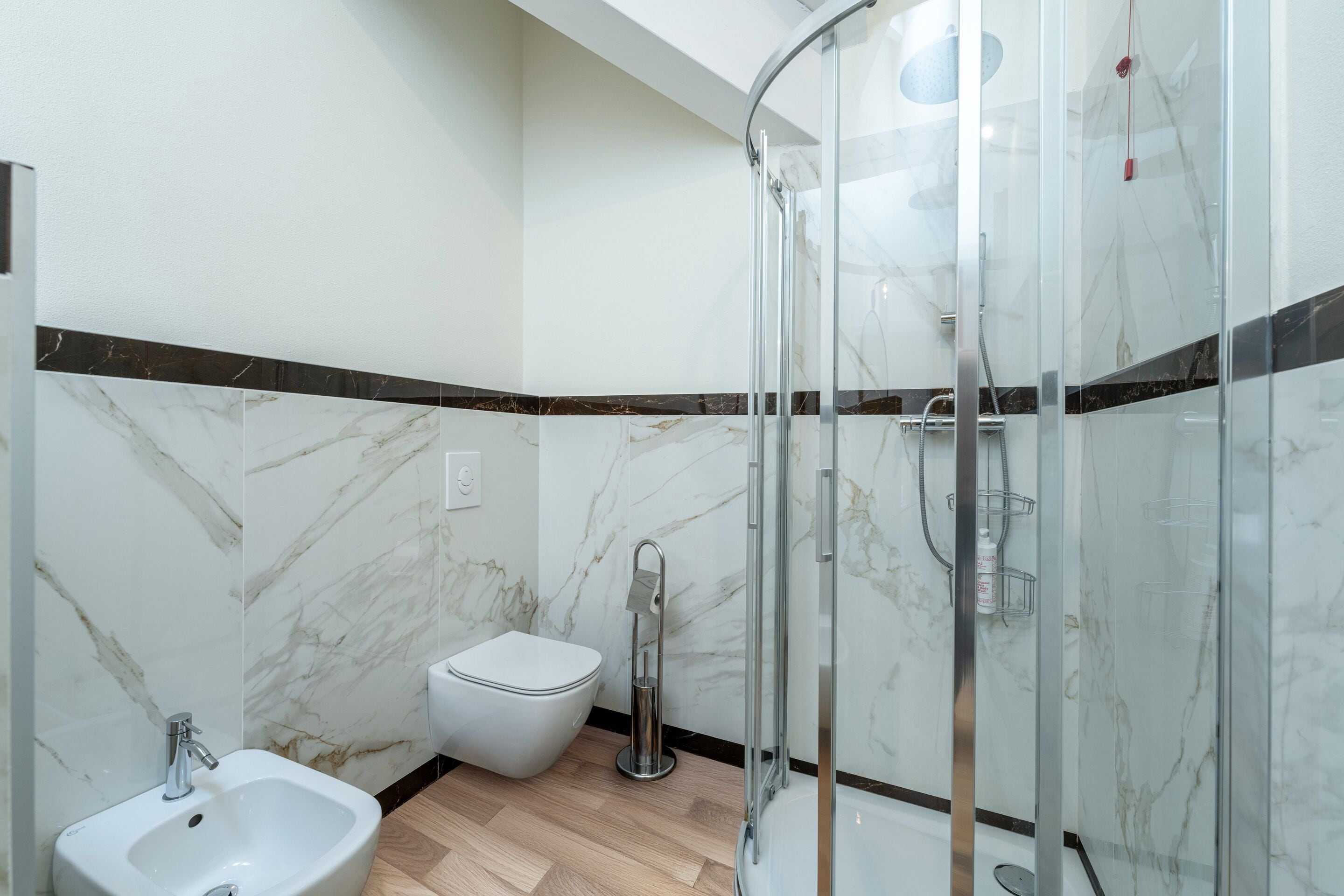 Ein modernes Badezimmer mit einer Duschkabine, einem weißen Waschbecken und einer Toilette.