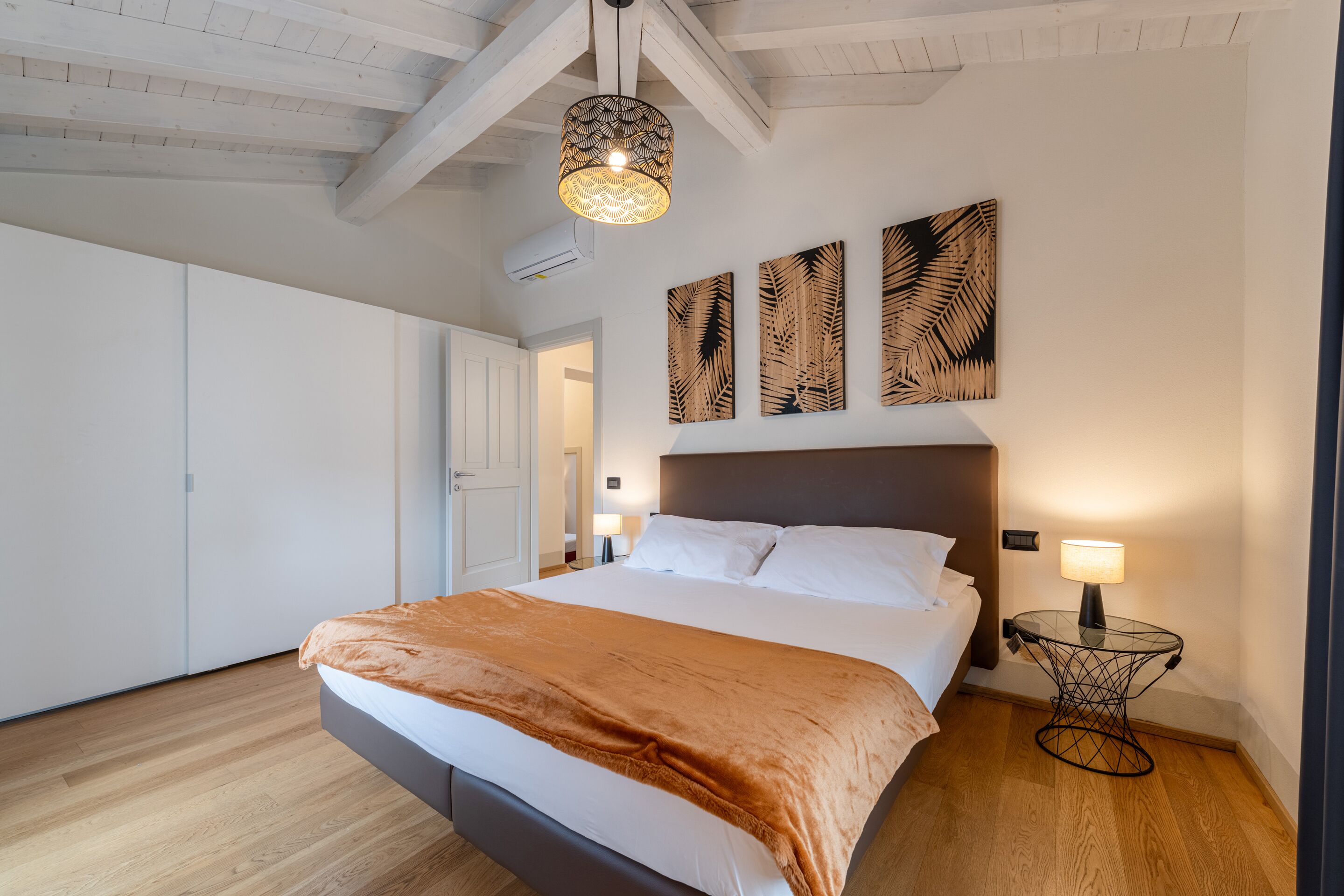 Een slaapkamer met een bed, een nachtkastje, een wandlamp en drie kunstwerken met bladmotieven.