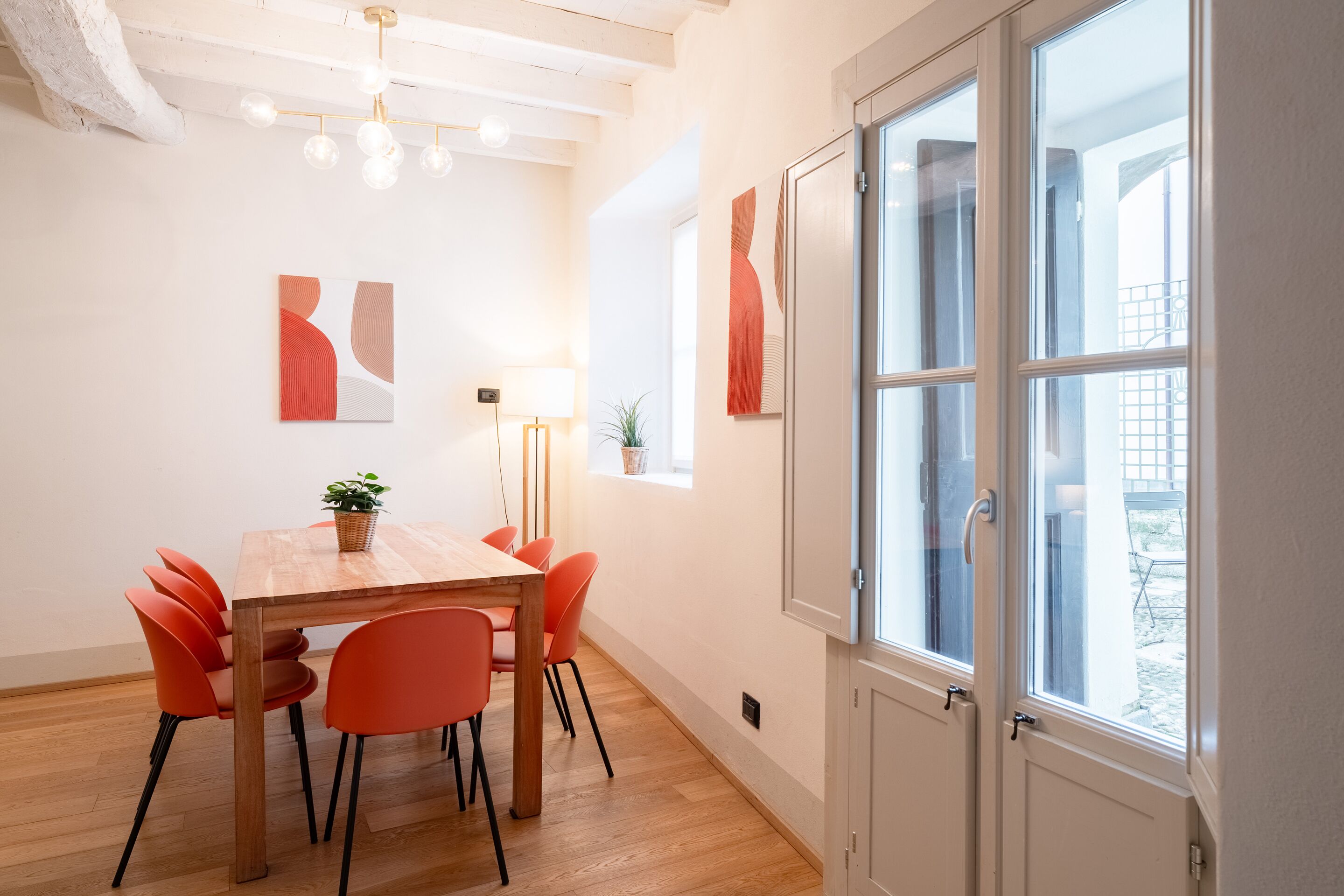 A dining area with a wooden table and orange chairs, a potted plant, and abstract wall art.