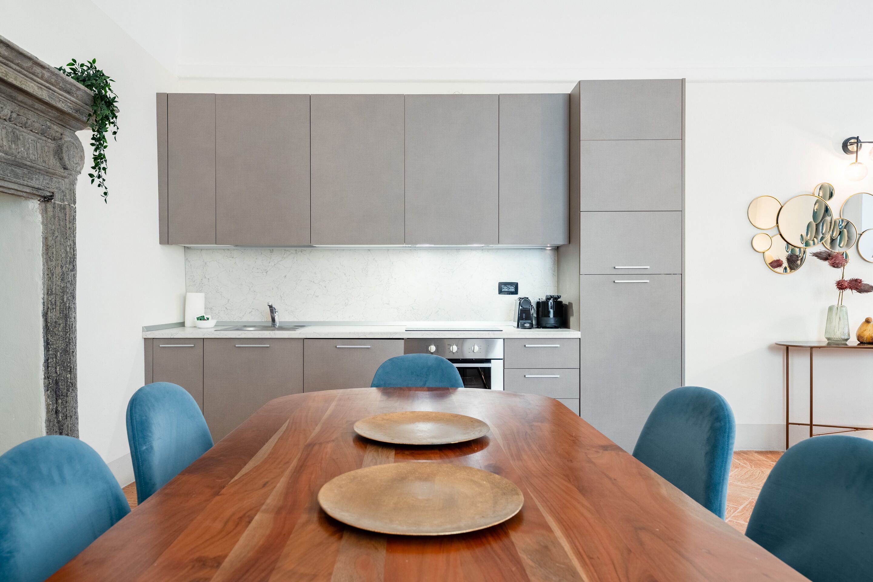 A modern kitchen with grey cabinets, a wooden dining table, and blue chairs.