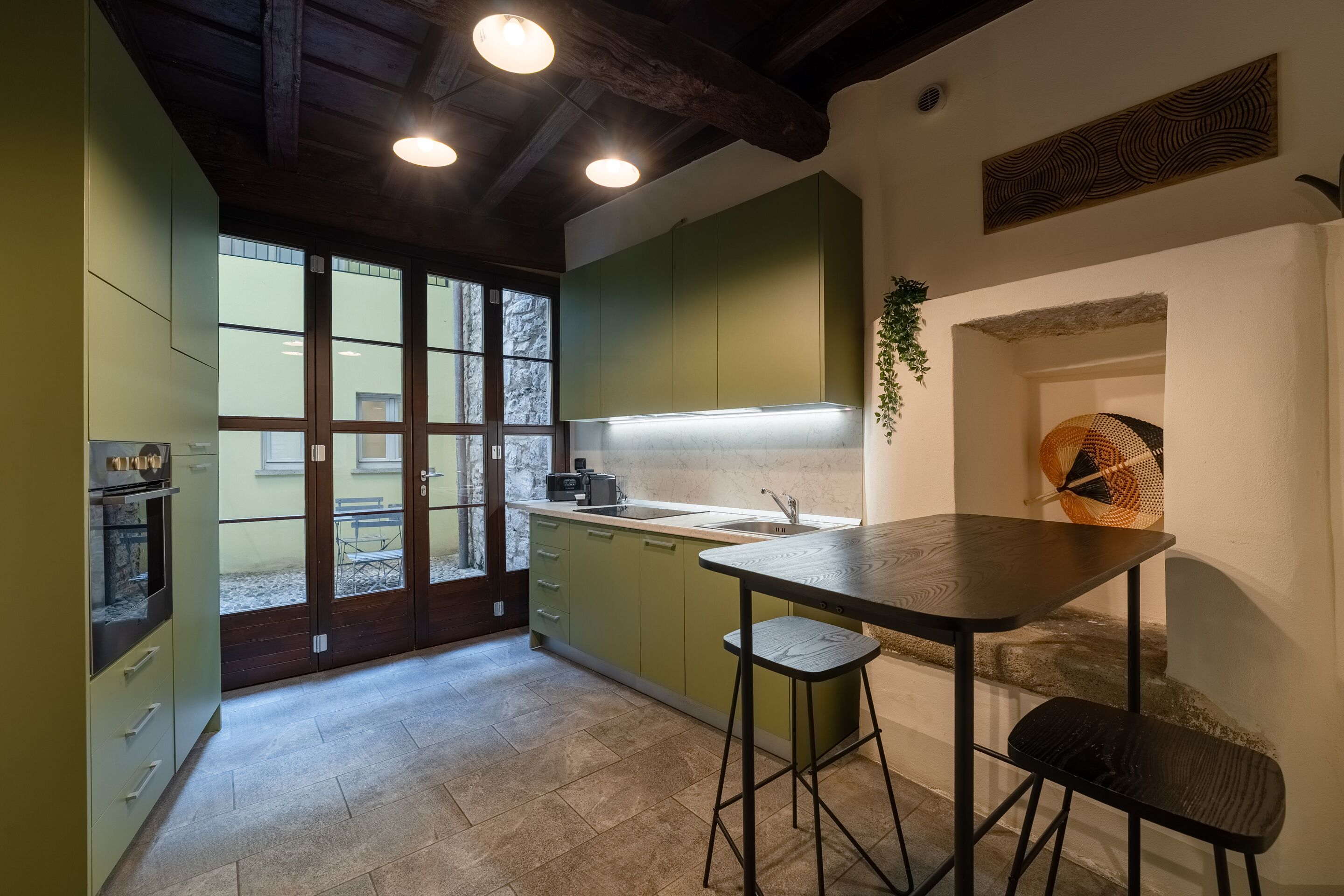 A modern kitchen with green cabinets, a marble countertop, and a bar stool.