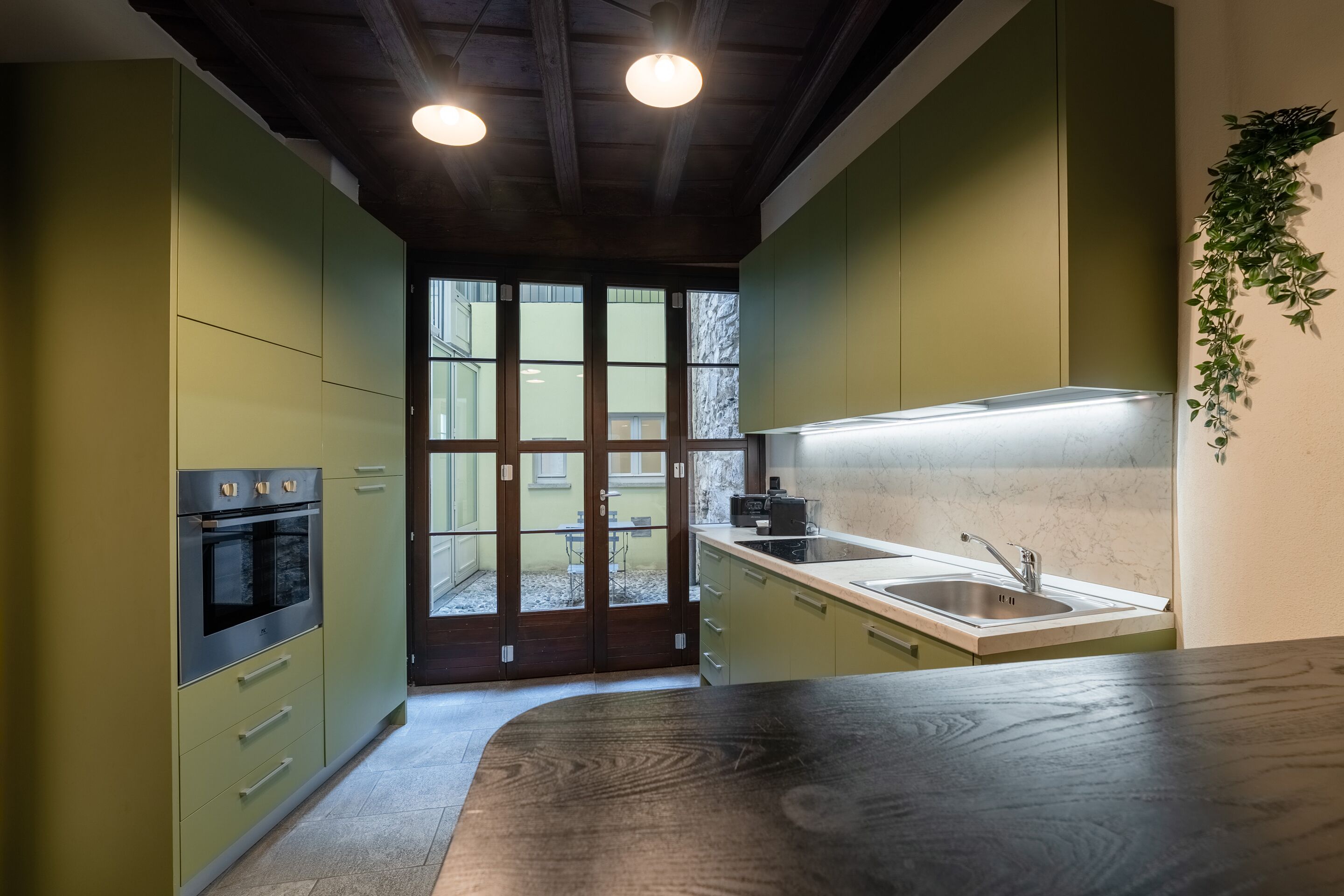 A modern kitchen with green cabinets, a wooden countertop, and a built-in oven.