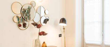 A room with a wall-mounted mirror arrangement, a small table with decorative items, and a floor lamp.