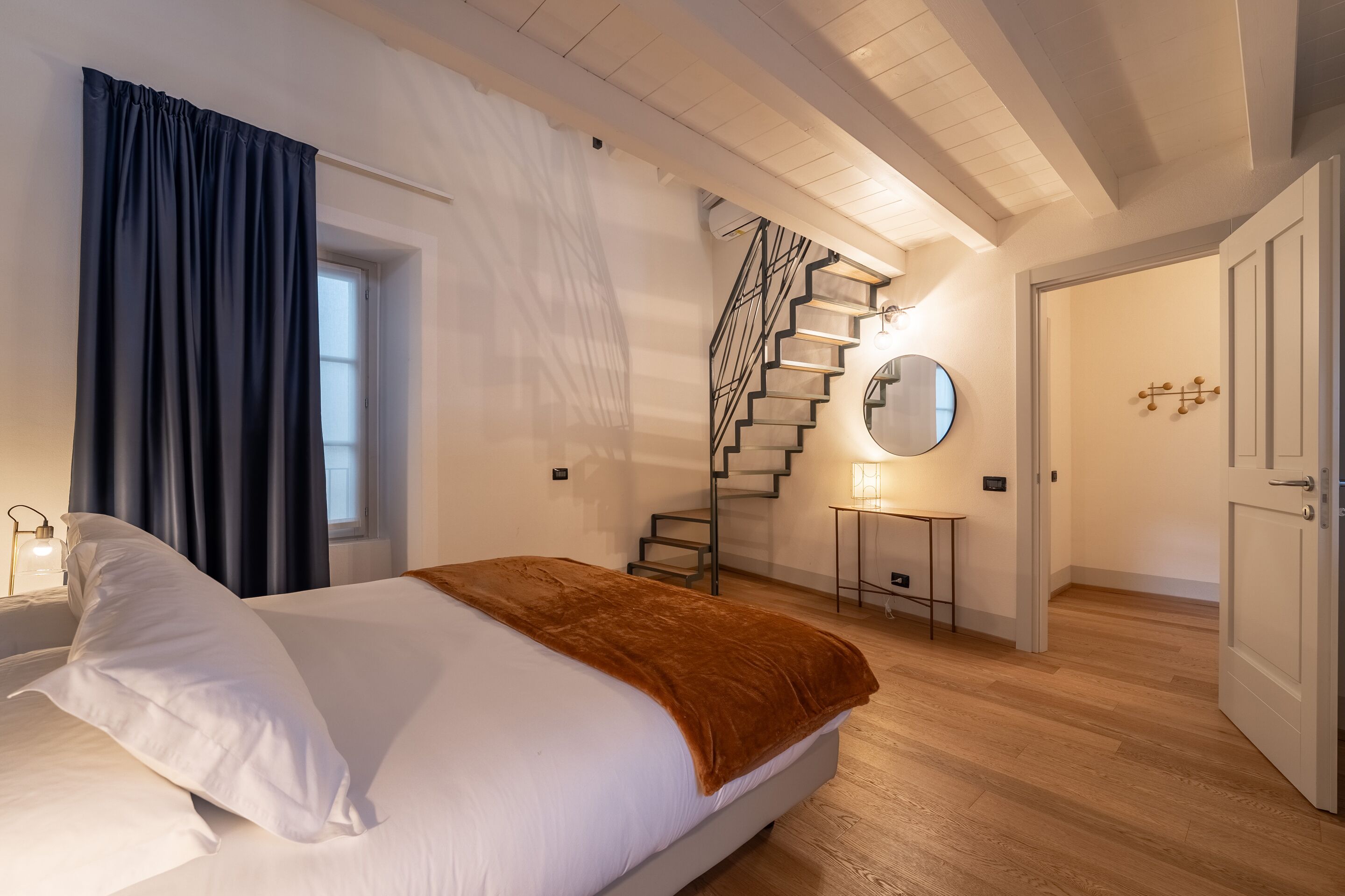 Een slaapkamer met een bed, een trap, een ronde spiegel en een deur.