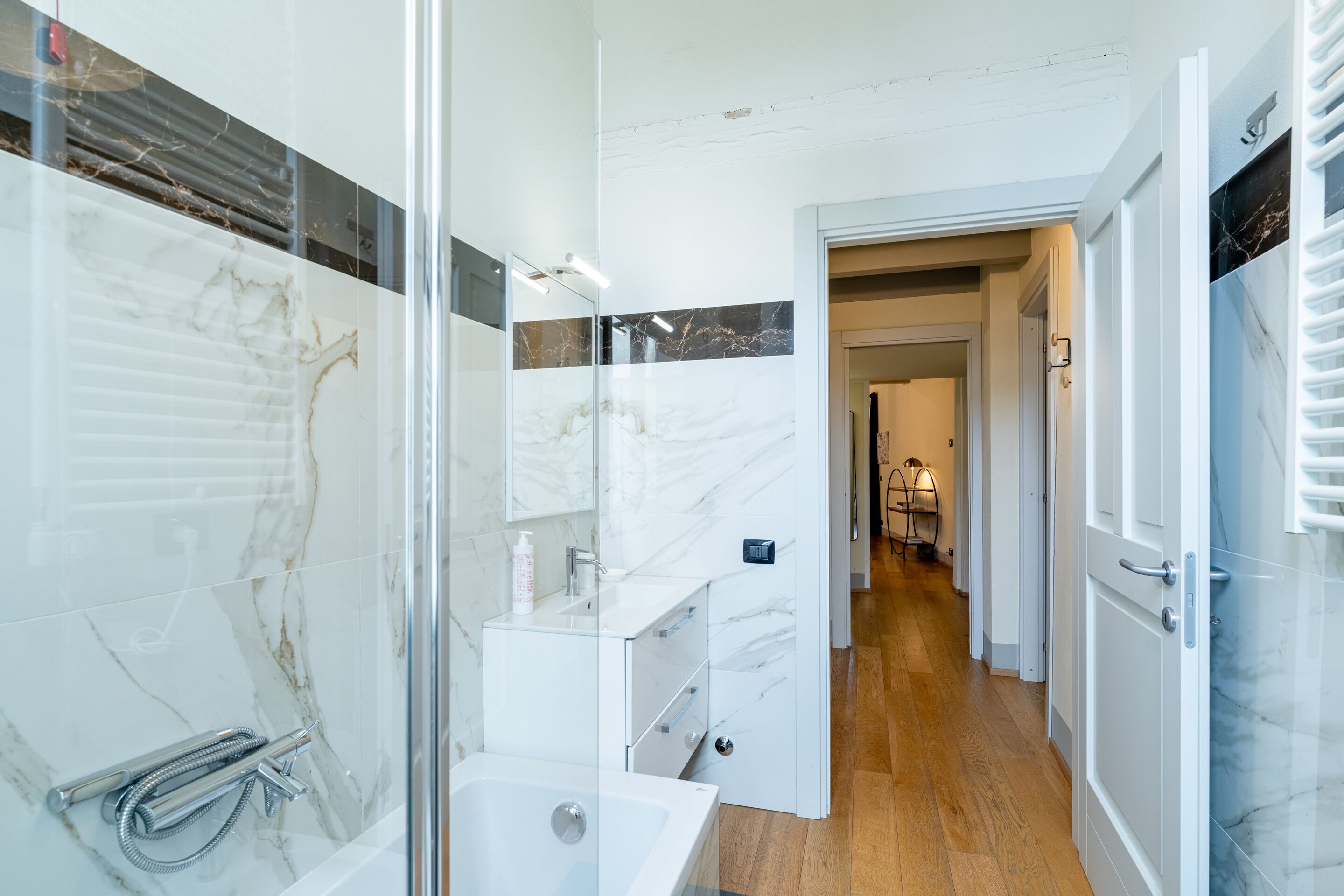 Un bagno moderno con cabina doccia in vetro, un lavandino bianco e una parete di mosaico in marmo.