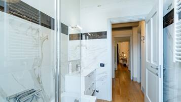 A modern bathroom with a glass-enclosed shower, a white sink, and a marble backsplash.