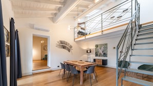 Un intérieur moderne avec une table à manger en bois, des chaises noires, un escalier et un espace en mezzanine.