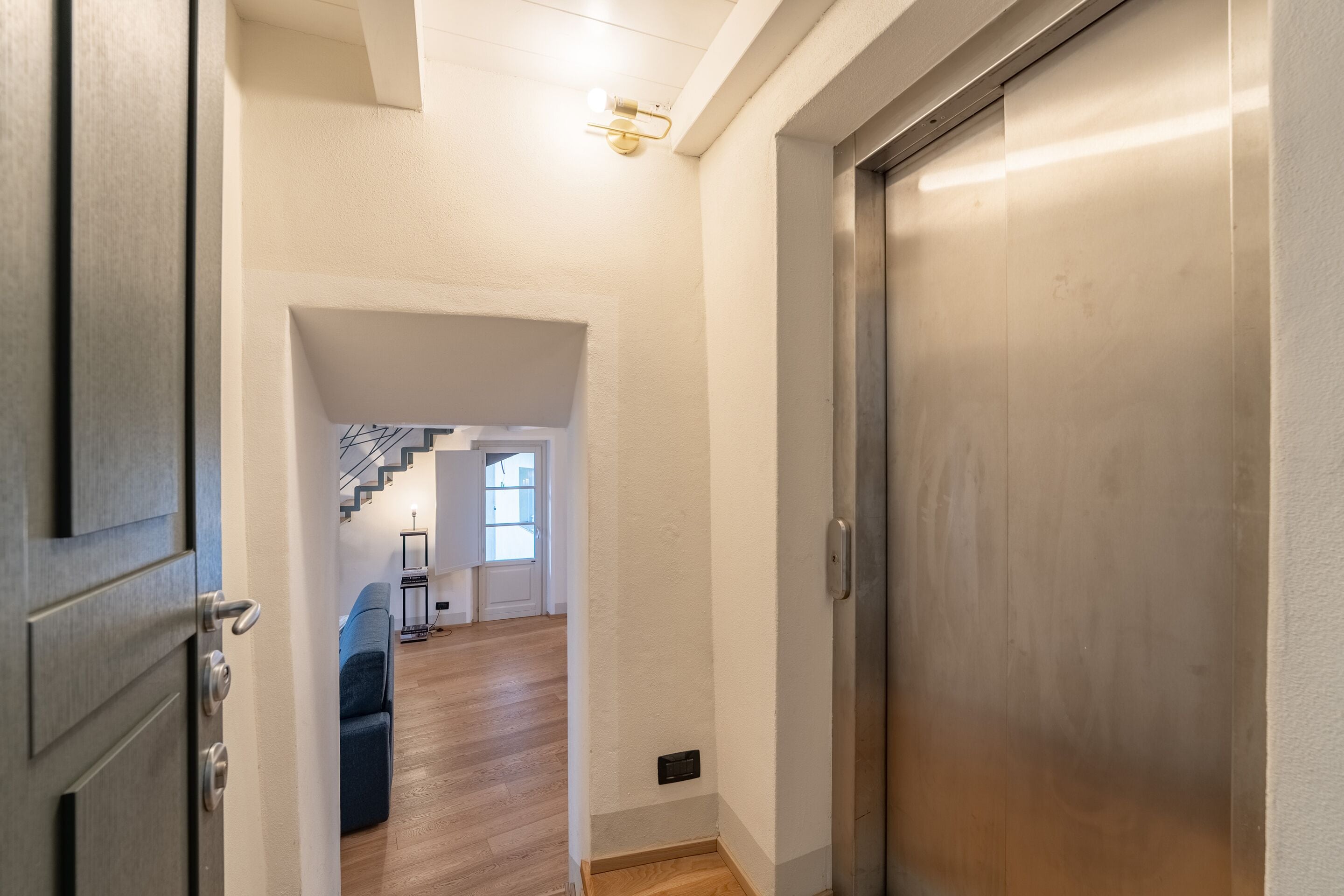 Un pasillo con piso de madera, una puerta cerrada a la derecha y una escalera que lleva a otra habitación.