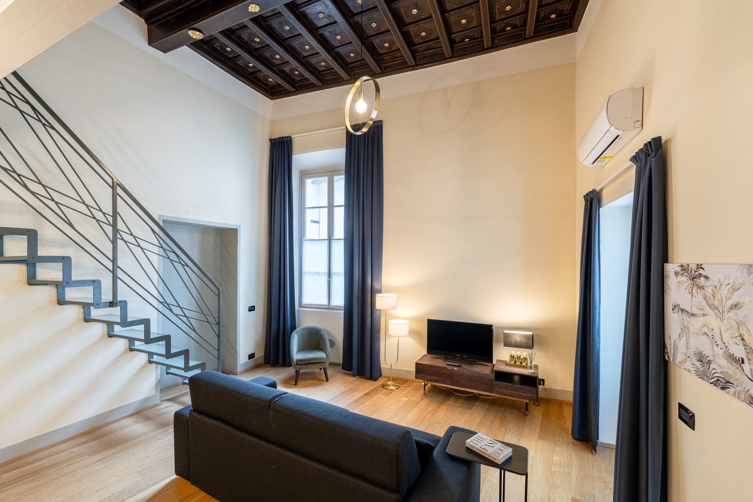 Ein modernes Wohnzimmer mit Treppe, einer Couch, einem Fernseher und einer Lampe.