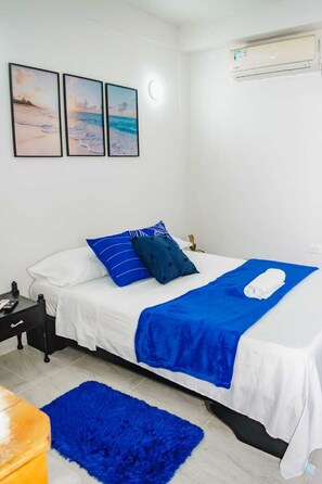 A bedroom with a bed, a nightstand, a blue rug, and three framed pictures on the wall. - Posada Cedar Valley  (Providencia)