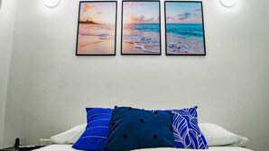 A bedroom with a bed, white bedding, and three framed pictures of a beach scene on the wall. - Posada Cedar Valley  (Providencia)