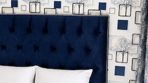 A bedroom with a tufted headboard, a bed with white bedding, and a wall with a geometric pattern of trees and squares. - Family - Elegant - Smart Home (Midrand)