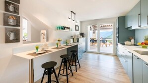 A modern kitchen with a central island, bar stools, and a dining area with a view. - Villa Les Adrets Mandelieu Hillside With Pool - 2303 (Fréjus)