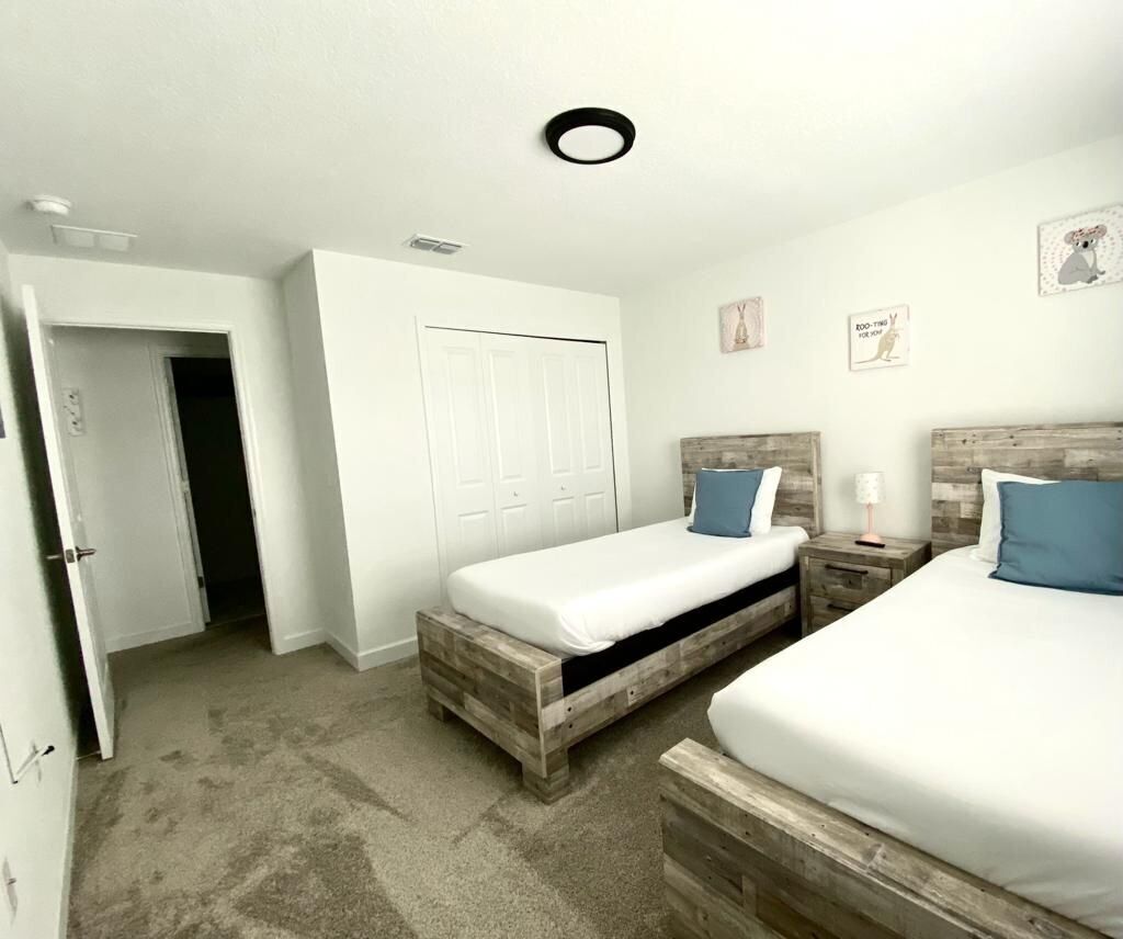 A bedroom with two beds, a white wardrobe, and a door leading to another room.