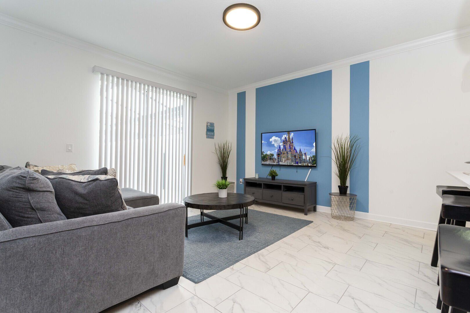 A modern living room with a grey sofa, a coffee table, and a flat-screen TV mounted on the wall.