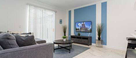 A modern living room with a grey sofa, a coffee table, and a flat-screen TV mounted on the wall.