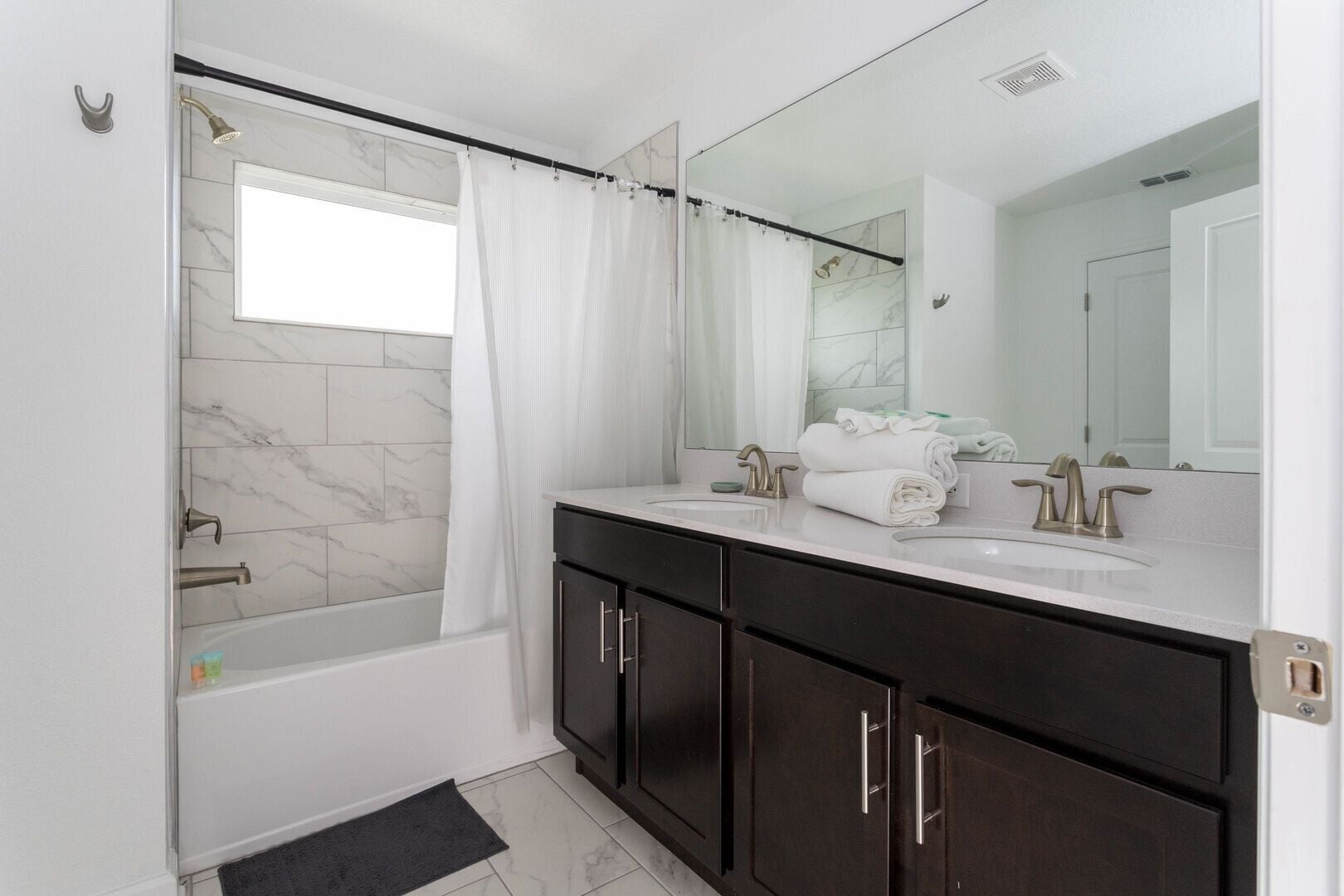 A modern bathroom with a bathtub, a large mirror, and dark wooden cabinets.