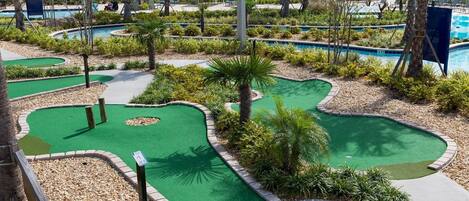 A miniature golf course with multiple holes, surrounded by lush greenery and a pool area.