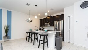 A modern kitchen with dark cabinets, a white island with bar stools, stainless steel appliances, and pendant lighting. - 4br/3ba Private Pool Storey Lake Resort Best Location Near Disney! (Kissimmee)