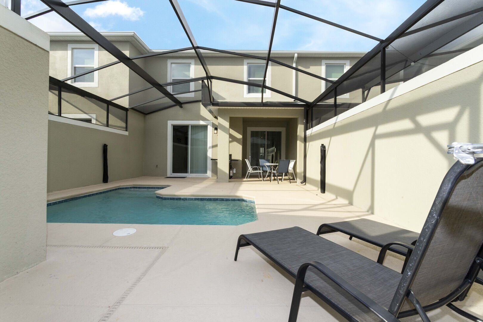 A covered outdoor swimming pool area with lounge chairs and a patio table.