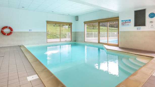 An indoor swimming pool with tiled walls, a lifebuoy, and a view of a grassy area through large windows.