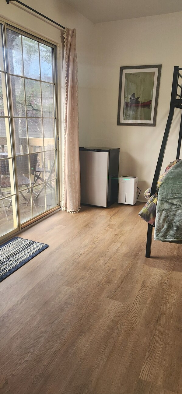Une pièce dotée d’une porte-fenêtre coulissante, d’une petite armoire blanche, d’un tableau encadré au mur et d’une chaise recouverte d’une couverture.