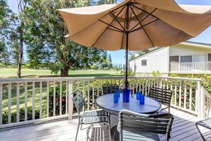 Eine Terrasse mit rundem Tisch und Stühlen, einem beigen Sonnenschirm und einem weißen Geländer.