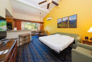 Ein Hotelzimmer mit einem Bett, einem Schreibtisch mit Fernseher, einem Sessel, einem kleinen Tisch und einem Fenster mit Vorhängen.
