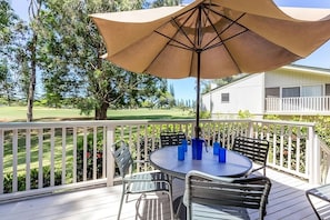 Eine Terrasse mit rundem Tisch und Stühlen, einem beigen Sonnenschirm und einem weißen Geländer.