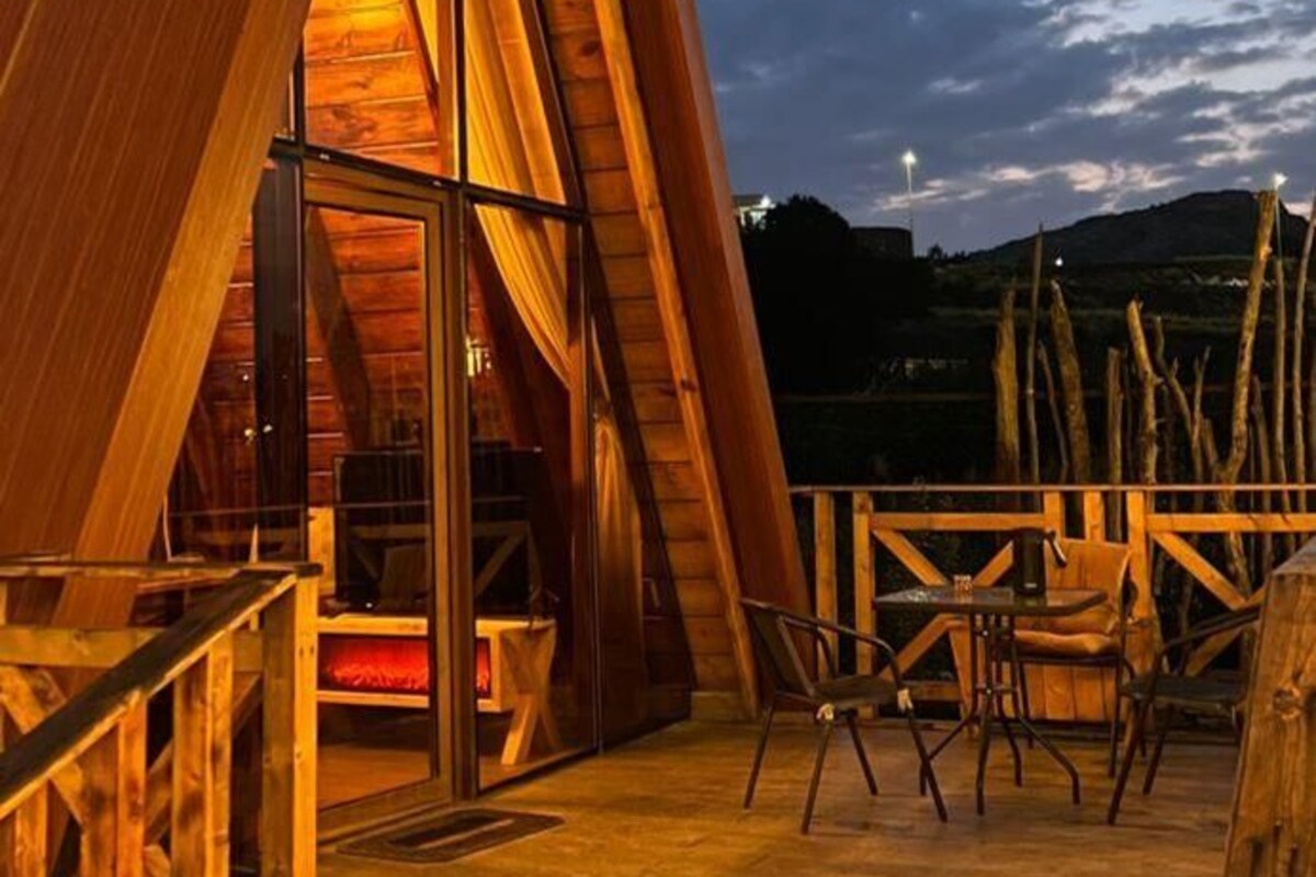 A wooden cabin with a sloped roof, a glass door entrance, and a patio area with outdoor seating.