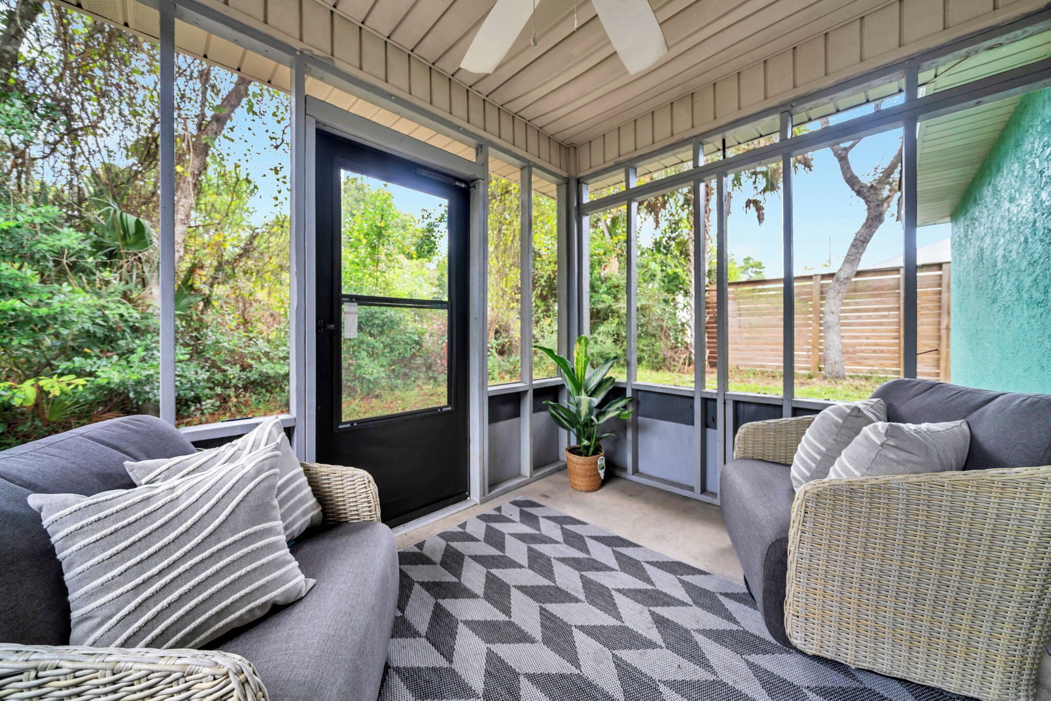 A covered outdoor seating area with a grey sofa, a wicker chair, and a potted plant.