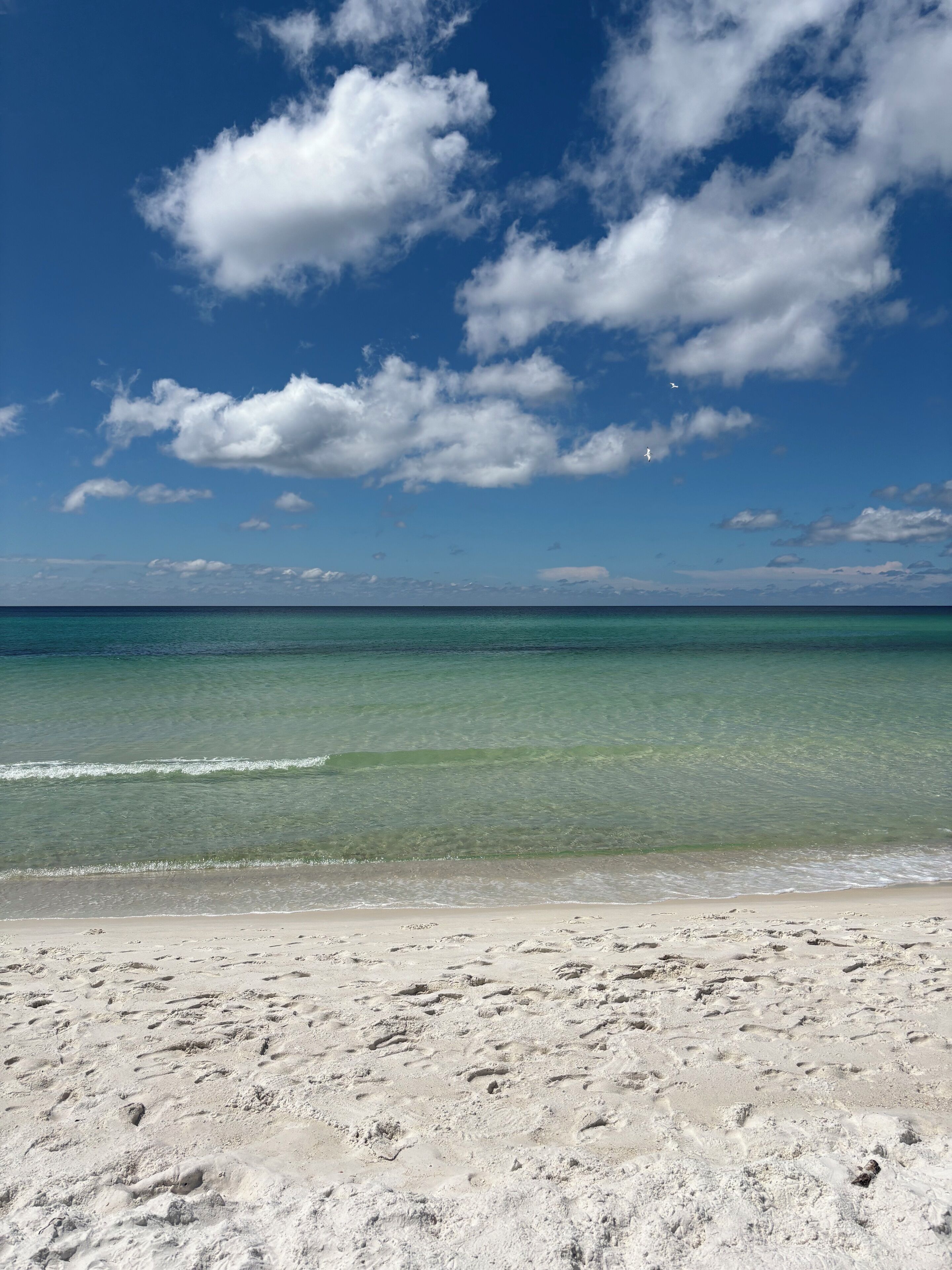 A beach with clear turquoise water, white sand, and a clear sky with clouds.