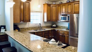 Una cocina con encimeras de granito, gabinetes de madera, electrodomésticos de acero inoxidable e iluminación colgante.