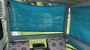 Une véranda avec deux chaises à motifs et une petite table, un moustiquaire bleu et une vue sur une pelouse verdoyante.