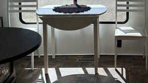 Une pièce avec une fenêtre donnant sur un beau paysage, une table, deux chaises et une étagère ornée d’objets décoratifs.