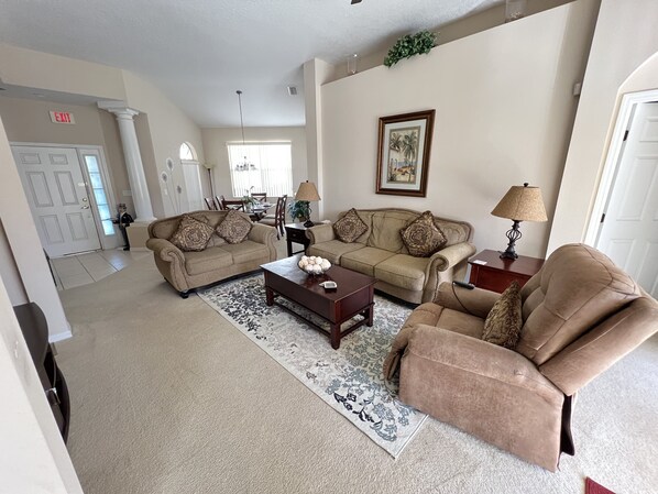 A living room with two sofas, a coffee table, and a lamp. There is a dining area in the background with a table and chairs.