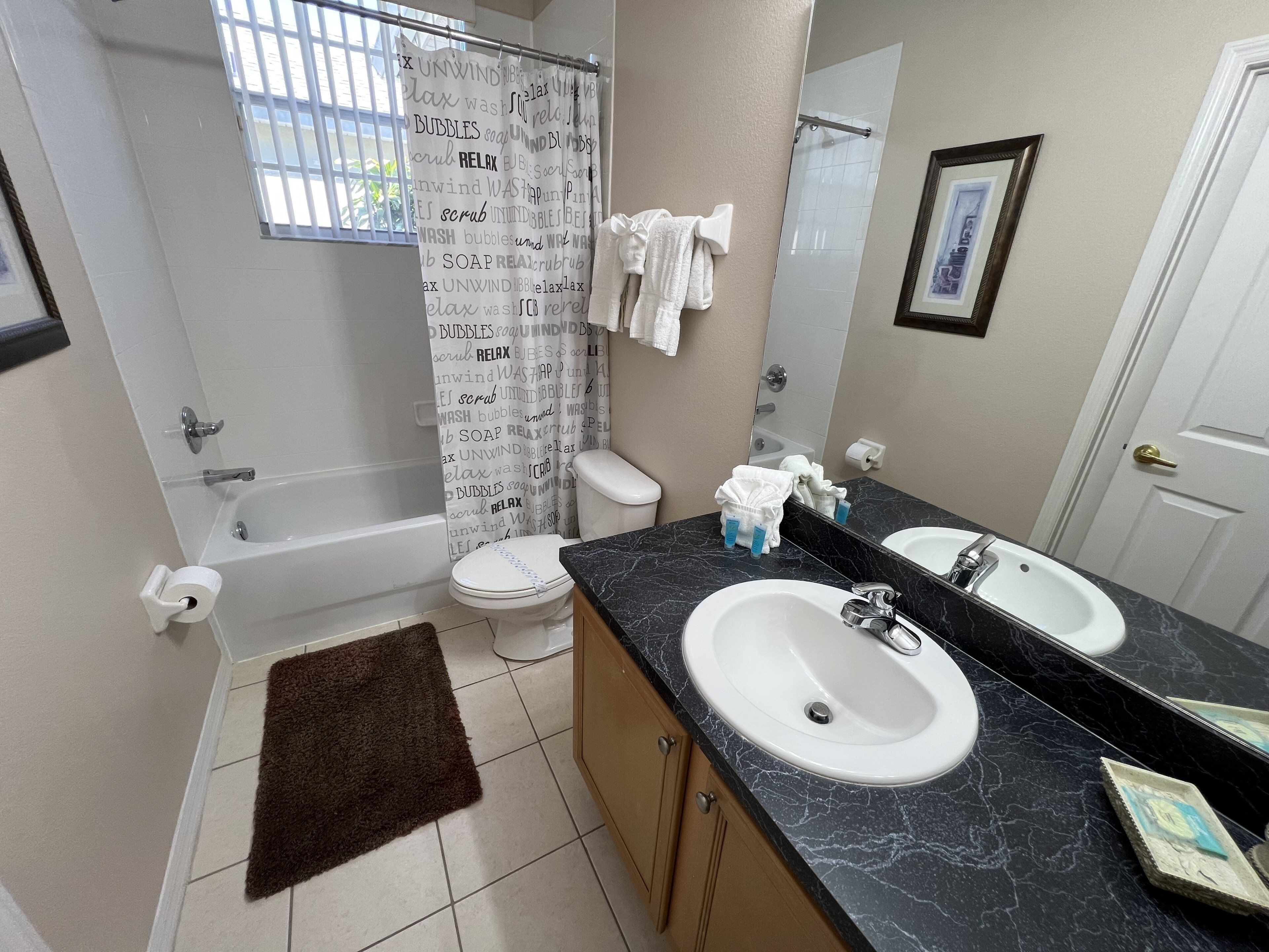 A bathroom with a bathtub, toilet, sink, and a shower curtain with text.