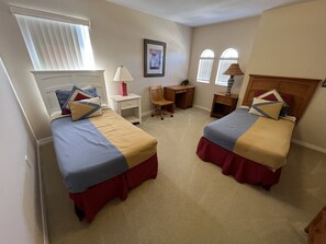 Een slaapkamer met twee bedden, een bureau, een stoel en een raam met jaloezieën.