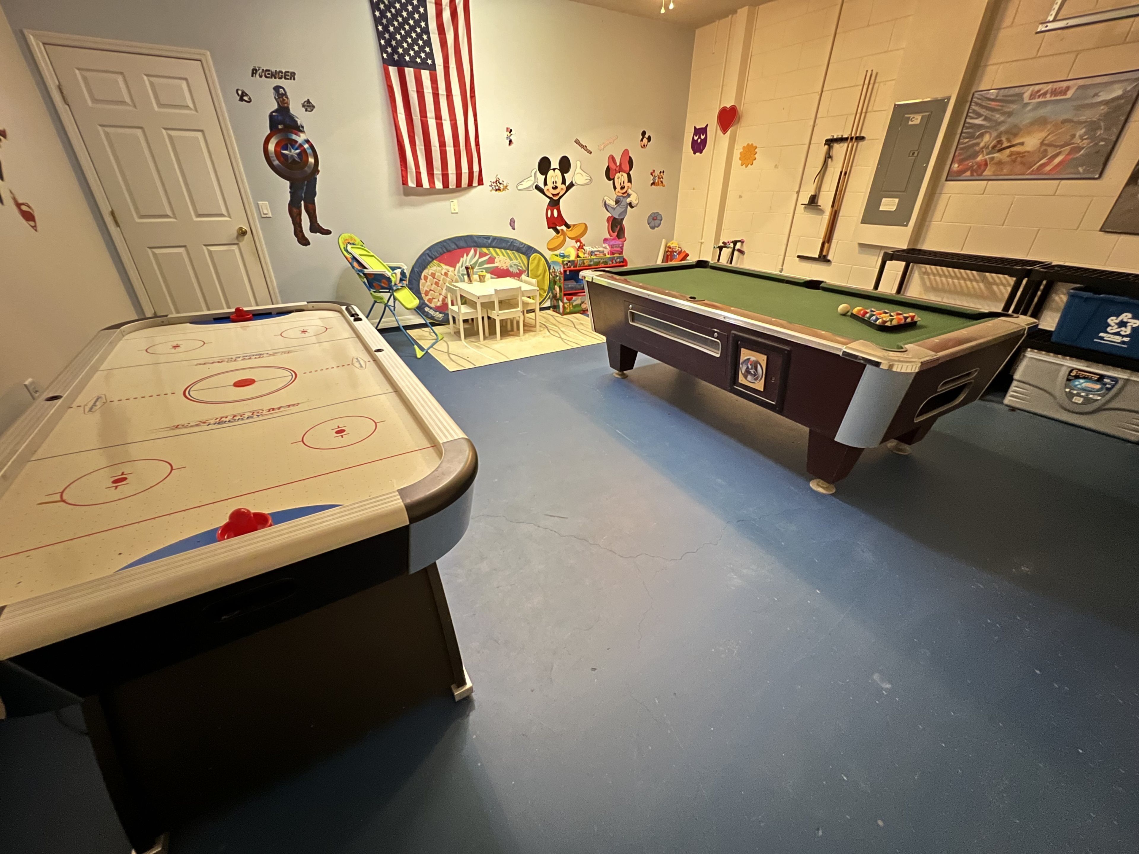 Een recreatieruimte met een luchthockeytafel, een pooltafel en een kleintje tafel met speelgoed.
