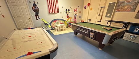 A recreational room with an air hockey table, a pool table, and a small table with toys.