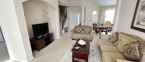 A spacious living room with a television, two sofas, a coffee table, and a staircase leading to another level.