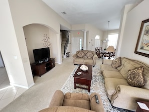 A spacious living room with a television, two sofas, a coffee table, and a staircase leading to another level.