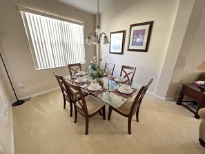 Een eethoek met een glazen tafel, houten stoelen en een vaas met bloemen.