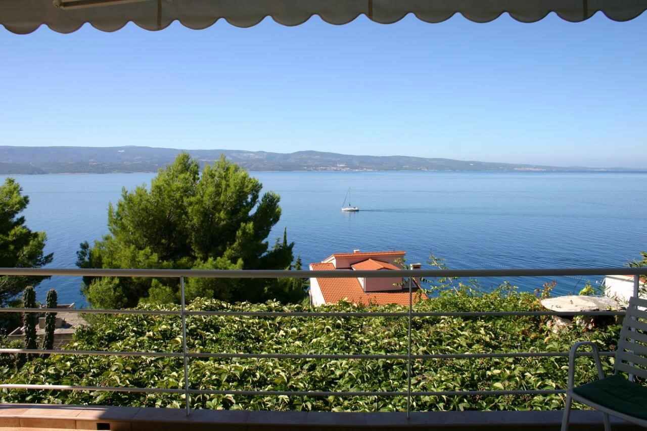 A balcony with a view of a calm sea, a distant boat, and a building with a red roof.