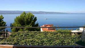 Un balcón con vista a un mar tranquilo, un barco a lo lejos y un edificio de techo rojo.